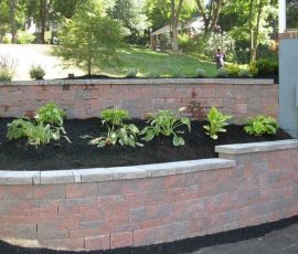 Two-tiered stone retaining wall with newly planted greenery and black mulch in a residential yard.