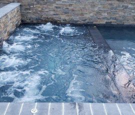 A rectangular hot tub with bubbling water is adjacent to a swimming pool, separated by a low tiled wall.