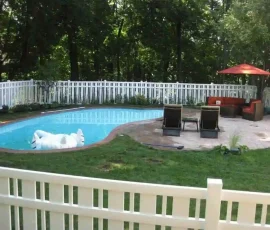 Backyard pool with a white inflatable, lounge chairs, patio furniture, and umbrella, surrounded by a white fence and trees.
