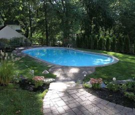 Oval swimming pool surrounded by grass and trees, with a stone path leading up to the water.